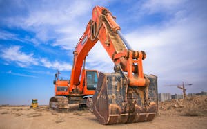 A large orange excavator working on a construction site under a blue sky.